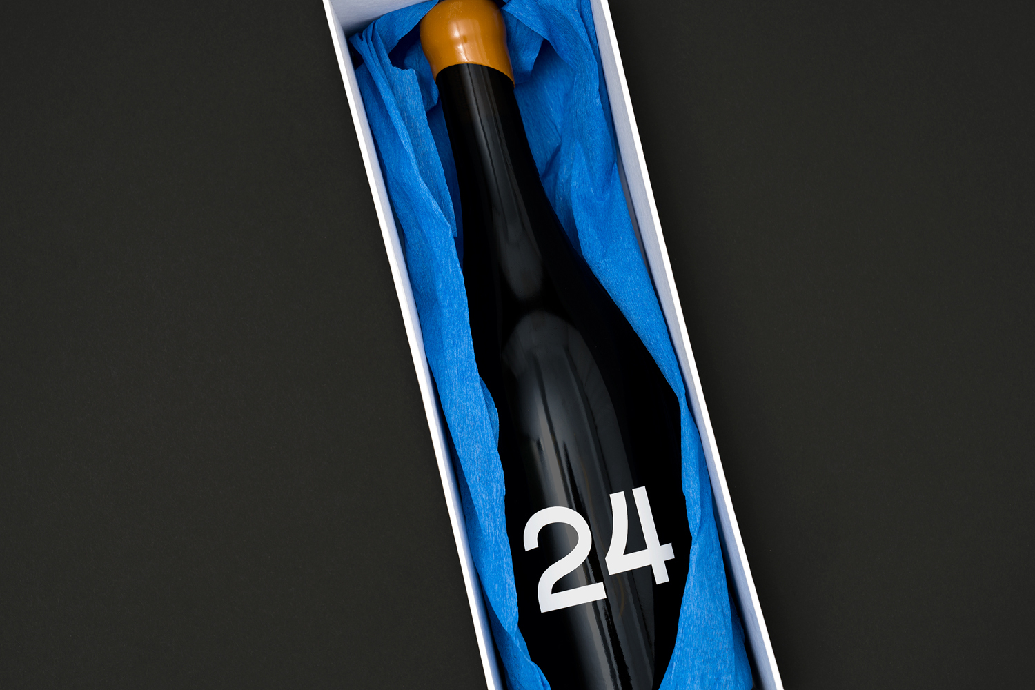 Dark glass wine bottle with number 24 in a white gift box lined with blue tissue paper