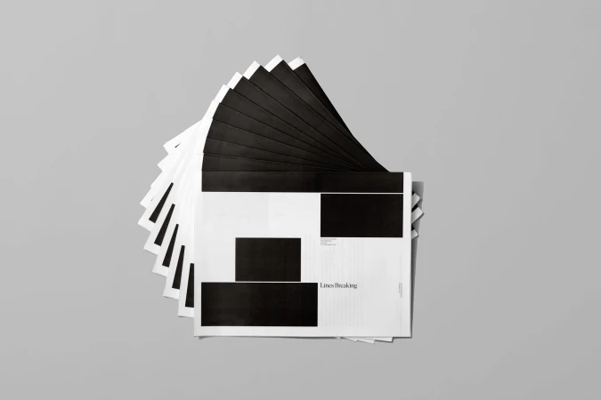 A fan of black and white printed paper sheets arranged in a circular overlapping stack on a neutral grey background