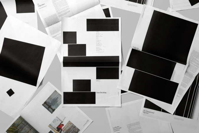 Overhead view of scattered black and white printed pages featuring bold black rectangular blocks and typography.