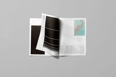 An open graphic publication with a curled page showing abstract black-and-white graphic lines, set against a plain grey backdrop.