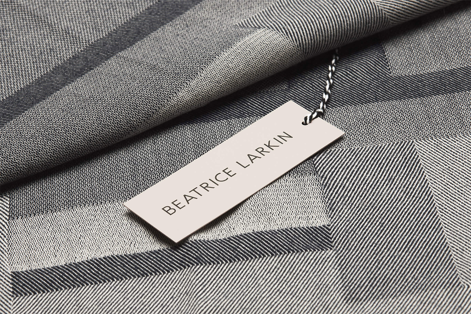 Beatrice Larkin brand label attached with string to a woven grey and black geometric patterned textile fabric.