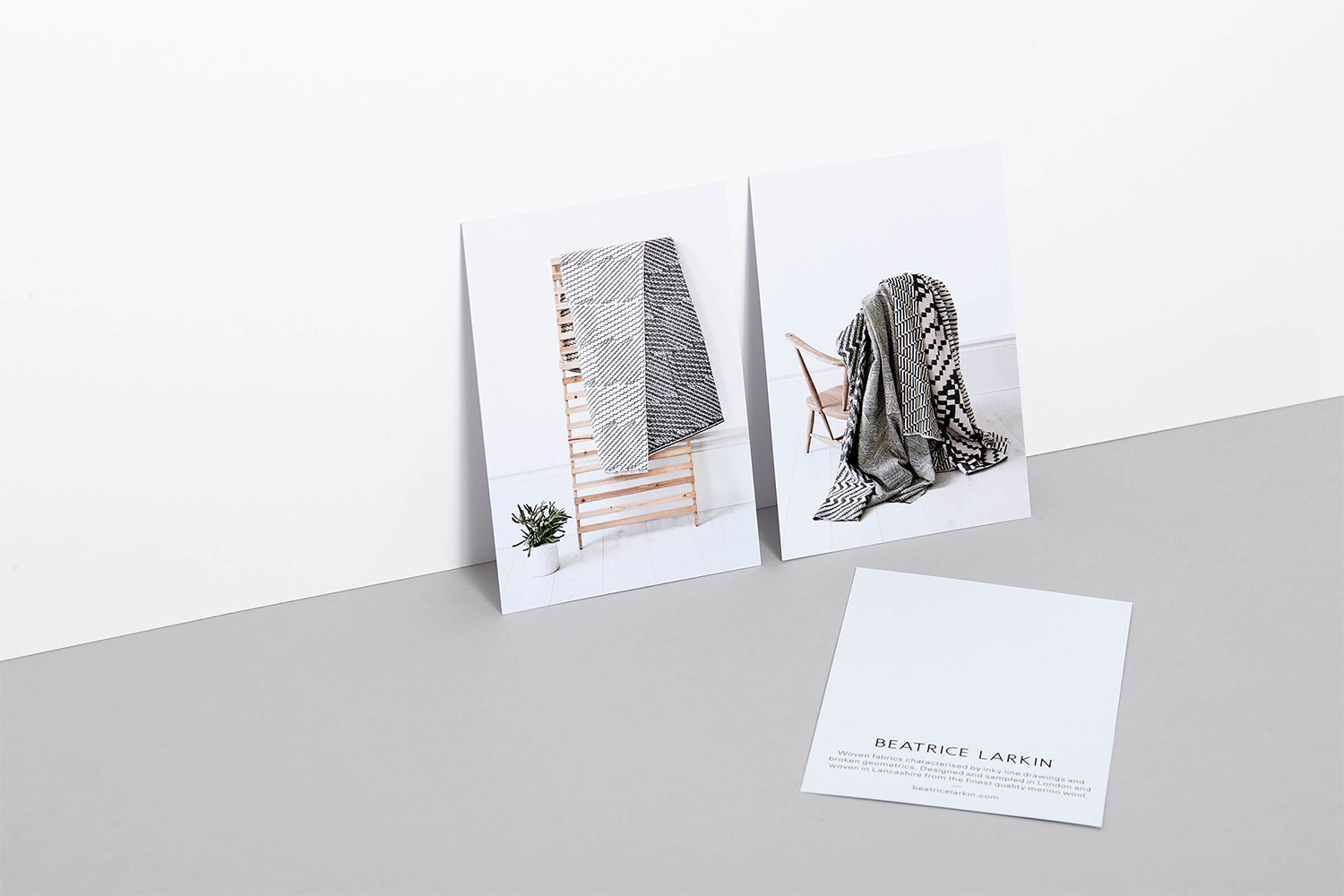 Three printed cards displaying black and white geometric patterned textiles leaning on a grey surface against a white wall.