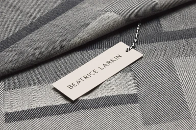 Beatrice Larkin brand label attached with string to a woven grey and black geometric patterned textile fabric.