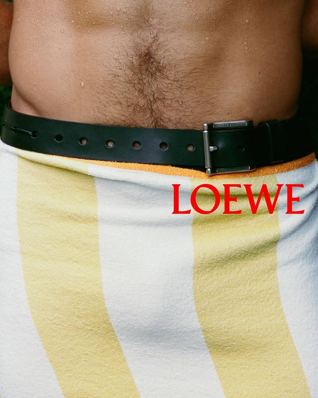 Close-up of a person wearing a black leather belt over a white and yellow striped towel for Loewe Pre-Spring 2026