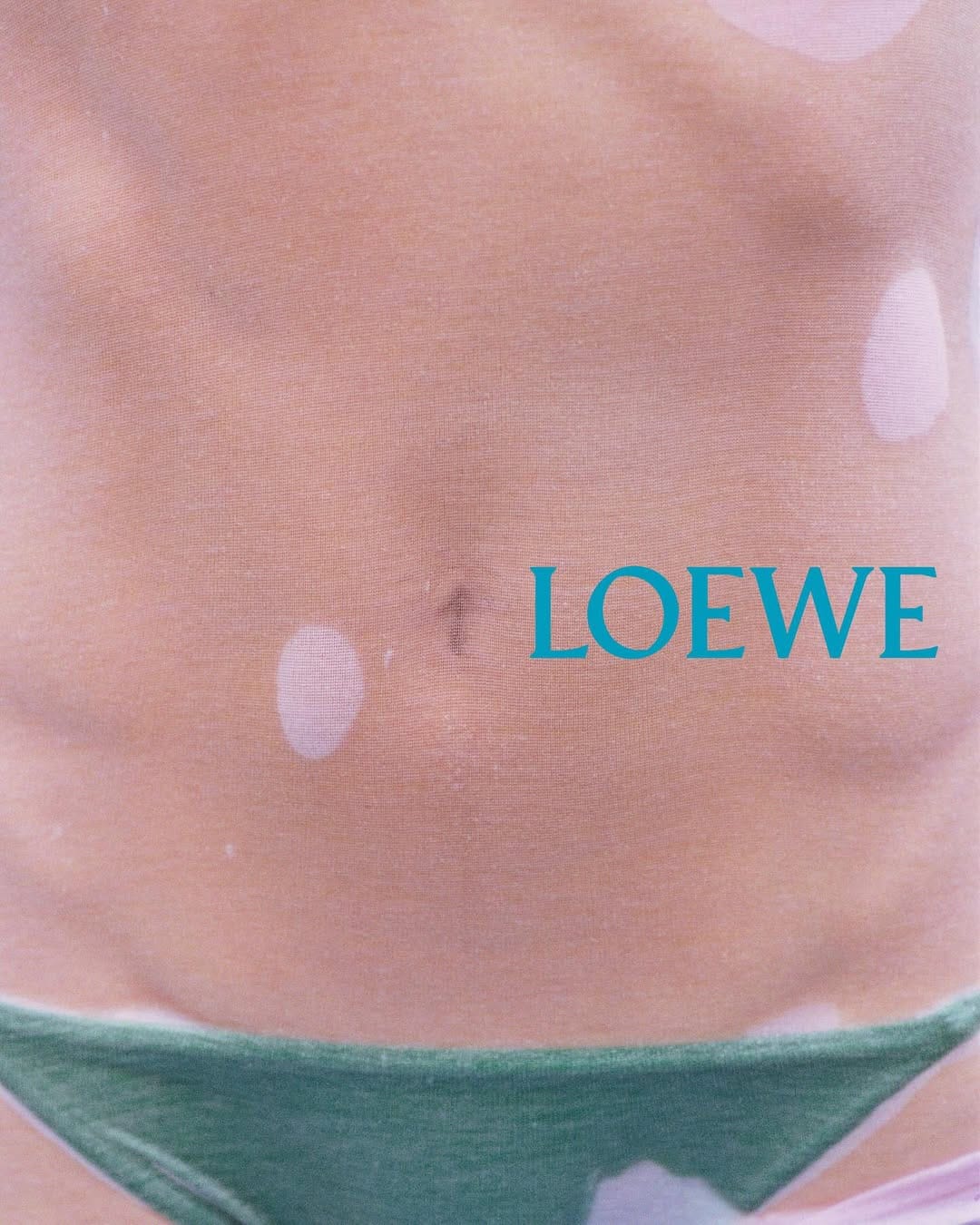 Close-up torso detail wearing dark green bikini bottoms with teal typography overlay for Loewe