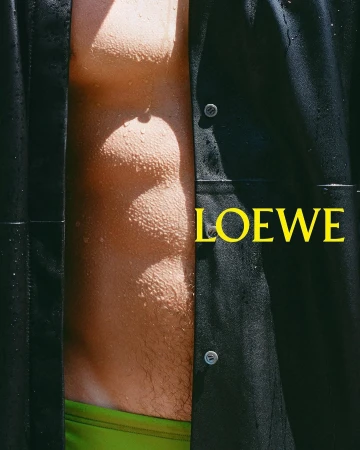 Close-up portrait of a man wearing an open black shirt and bright green swim shorts with water droplets on skin for Loewe.