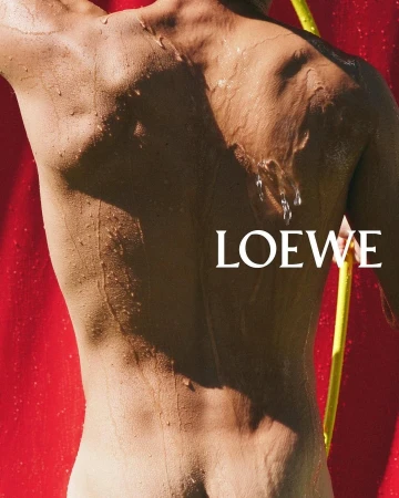 Close-up portrait of a wet person's back against a bright red backdrop with white Loewe text and a yellow pole