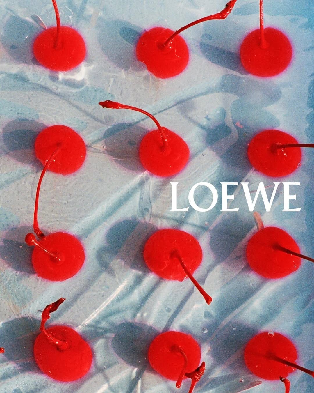 Top-down view of bright red cherries arranged in a grid pattern on a pale translucent blue surface with visible shadows