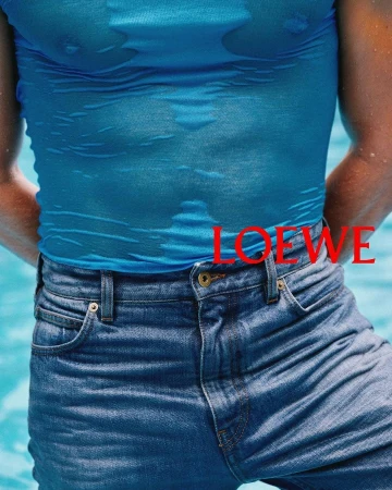 Close-up of a person wearing a bright blue wet top and blue denim jeans against a water background with red LOEWE text.