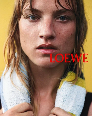 Close-up portrait of a model with wet hair and a towel around the neck against a yellow background, Loewe ad