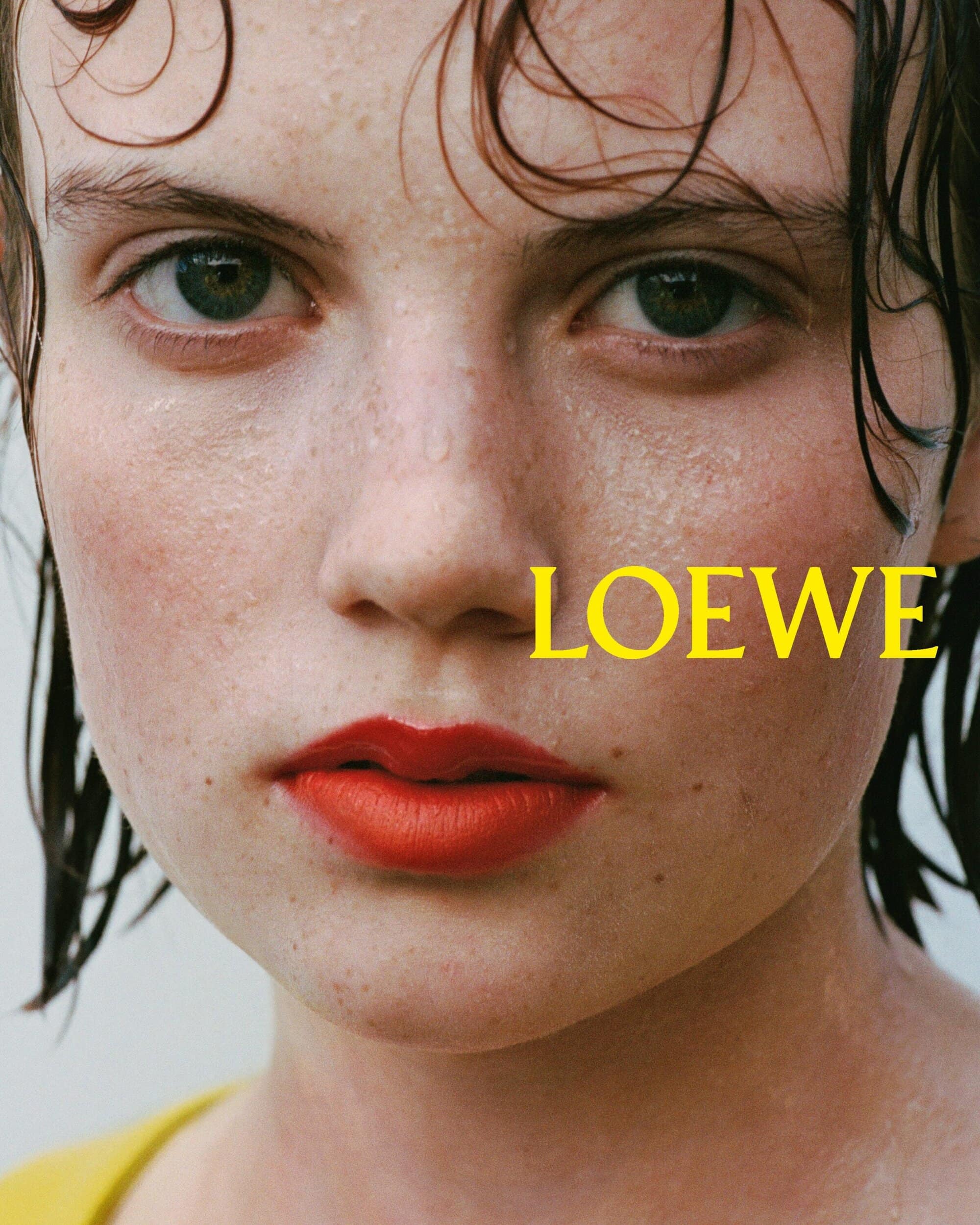 Close-up portrait of a woman with wet hair, freckles, and red lipstick for Loewe Pre-Spring 2026 ad campaign