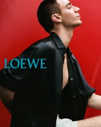 Man in a black leather shirt posing against a bold red background with turquoise Loewe typography