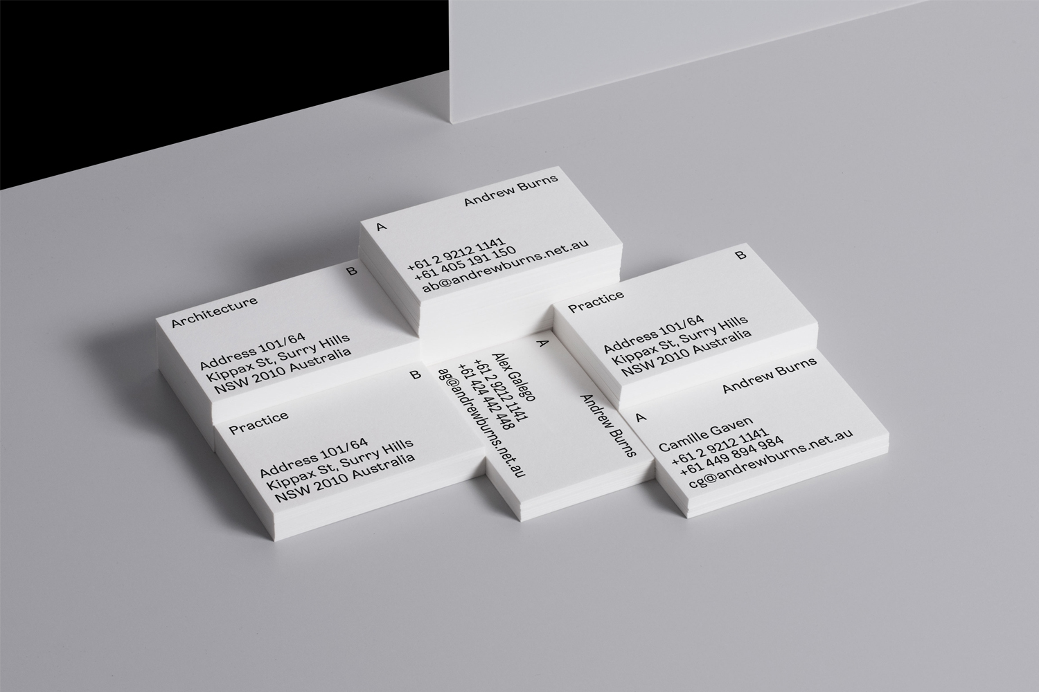 Stacks of white business cards with minimalist black typography arranged symmetrically on a grey surface.