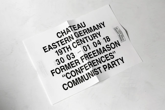 Folded white poster with bold black typography placed on a light textured surface.