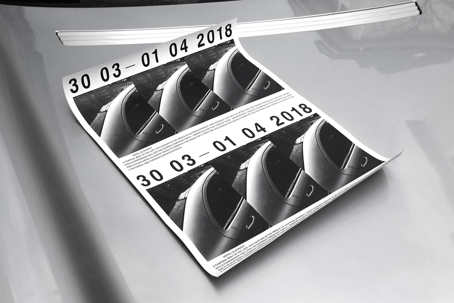 Monochrome poster with dates and car imagery resting on a metallic car surface