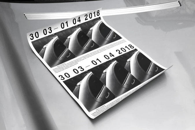 Monochrome poster with dates and car imagery resting on a metallic car surface