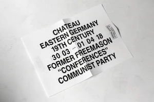 Folded white poster with bold black typography placed on a light textured surface.