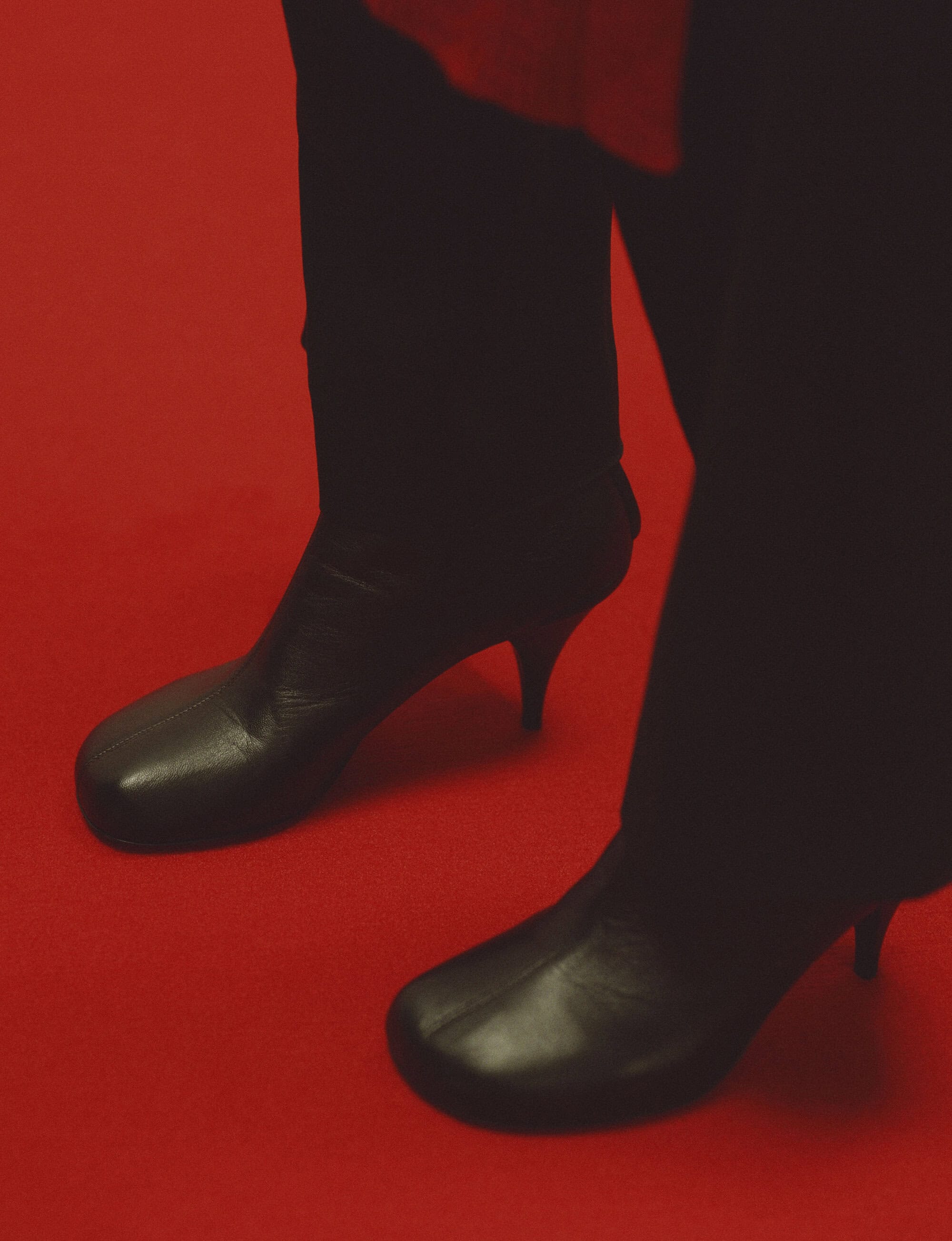 Close up of person wearing black leather boots and dark trousers standing on a red carpet