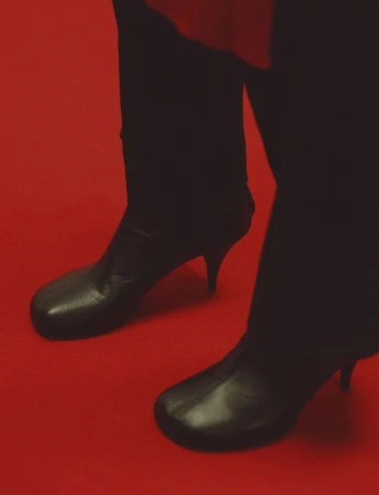 Close up of person wearing black leather boots and dark trousers standing on a red carpet