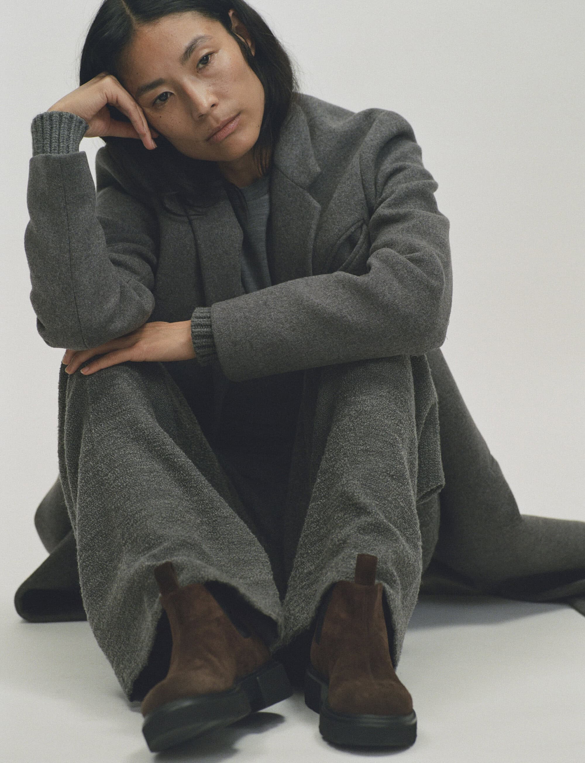 Woman sitting on the floor wearing a grey wool blazer and matching trousers with brown boots