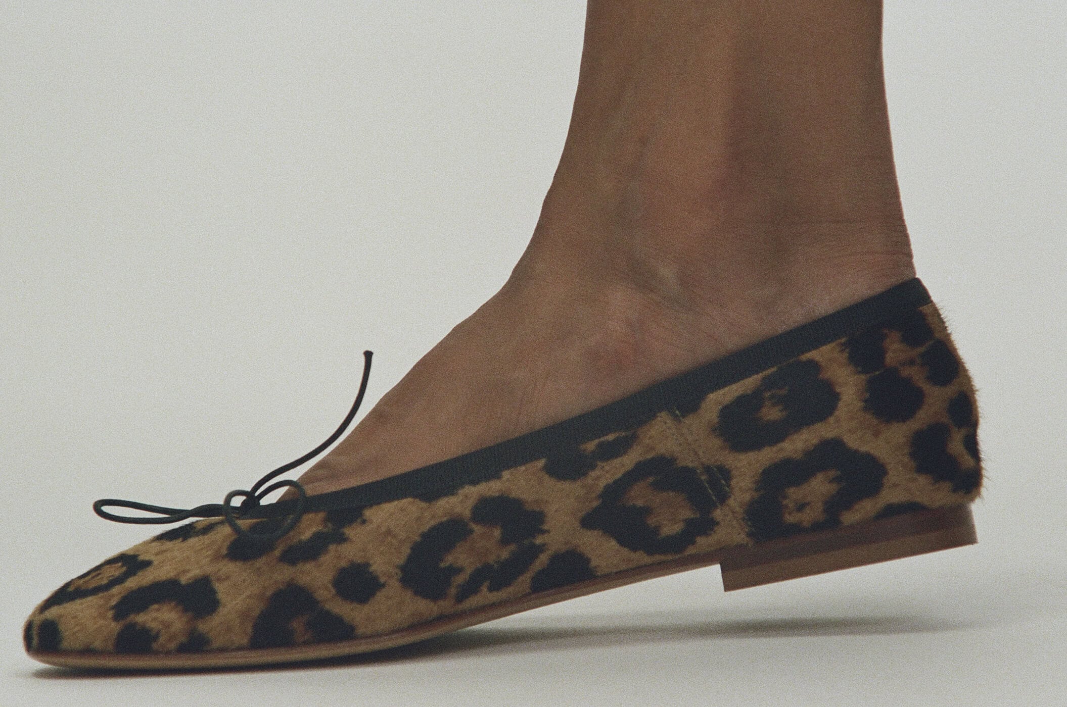 Close-up profile of a leopard print calf hair flat shoe worn on a foot against a plain light grey background