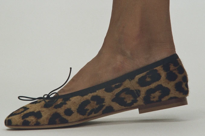 Close-up profile of a leopard print calf hair flat shoe worn on a foot against a plain light grey background