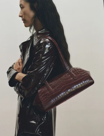 Profile view of a woman wearing a glossy patent leather coat carrying a burgundy leather shoulder bag