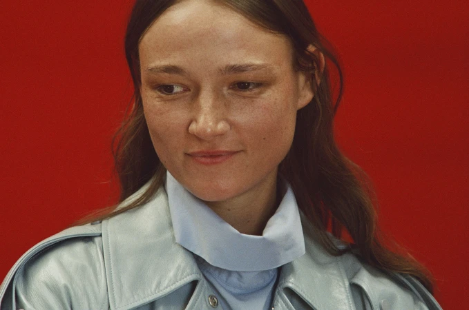 Close-up portrait of a woman wearing a light blue leather jacket against a vibrant red backdrop for Mansur Gavriel Fall 2025.