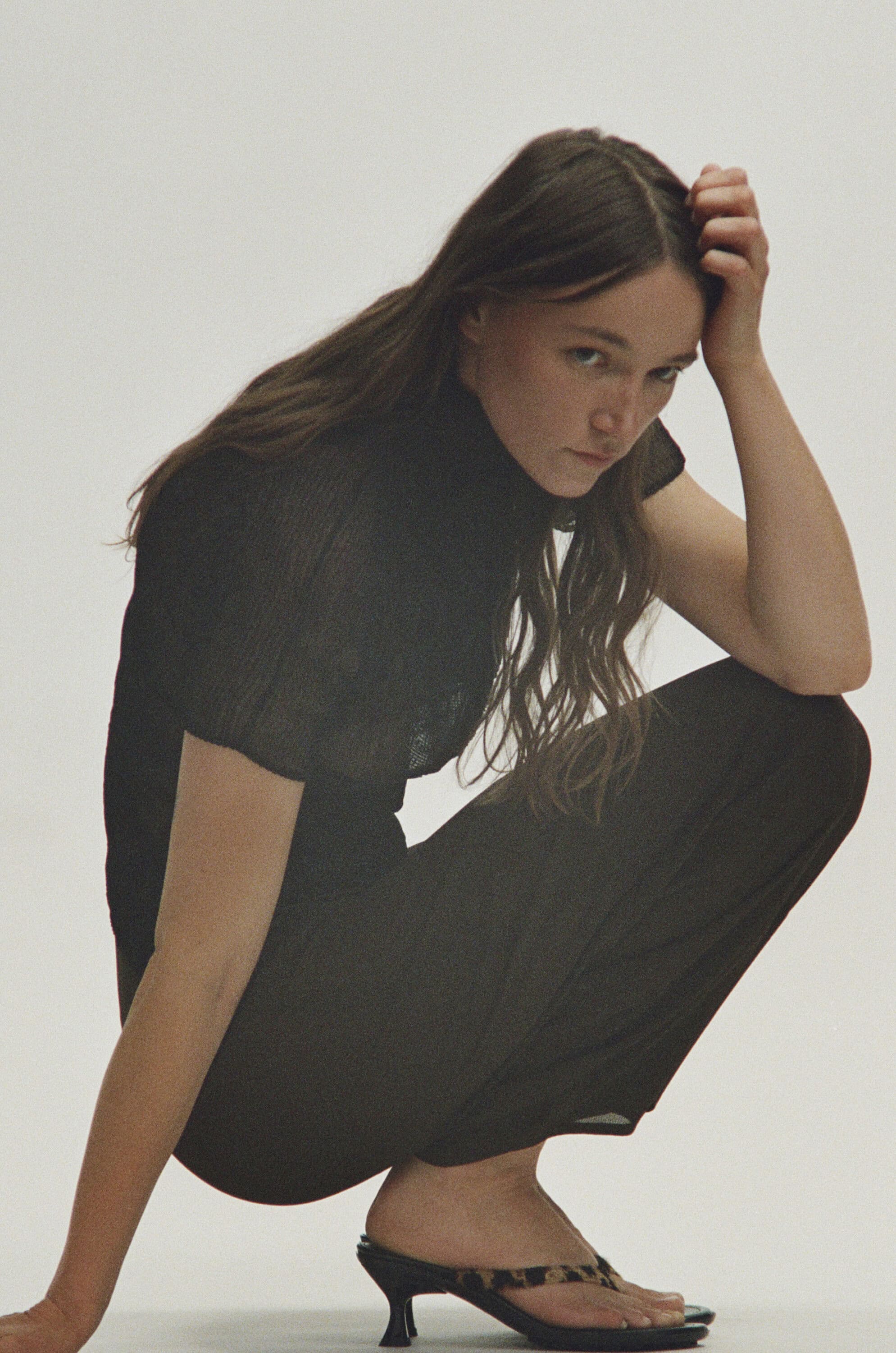 Woman wearing a black top and trousers crouching against a seamless white background