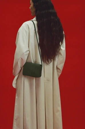 Model wearing a white coat and dark green shoulder bag against a vibrant red background in a Mansur Gavriel fall campaign ad.