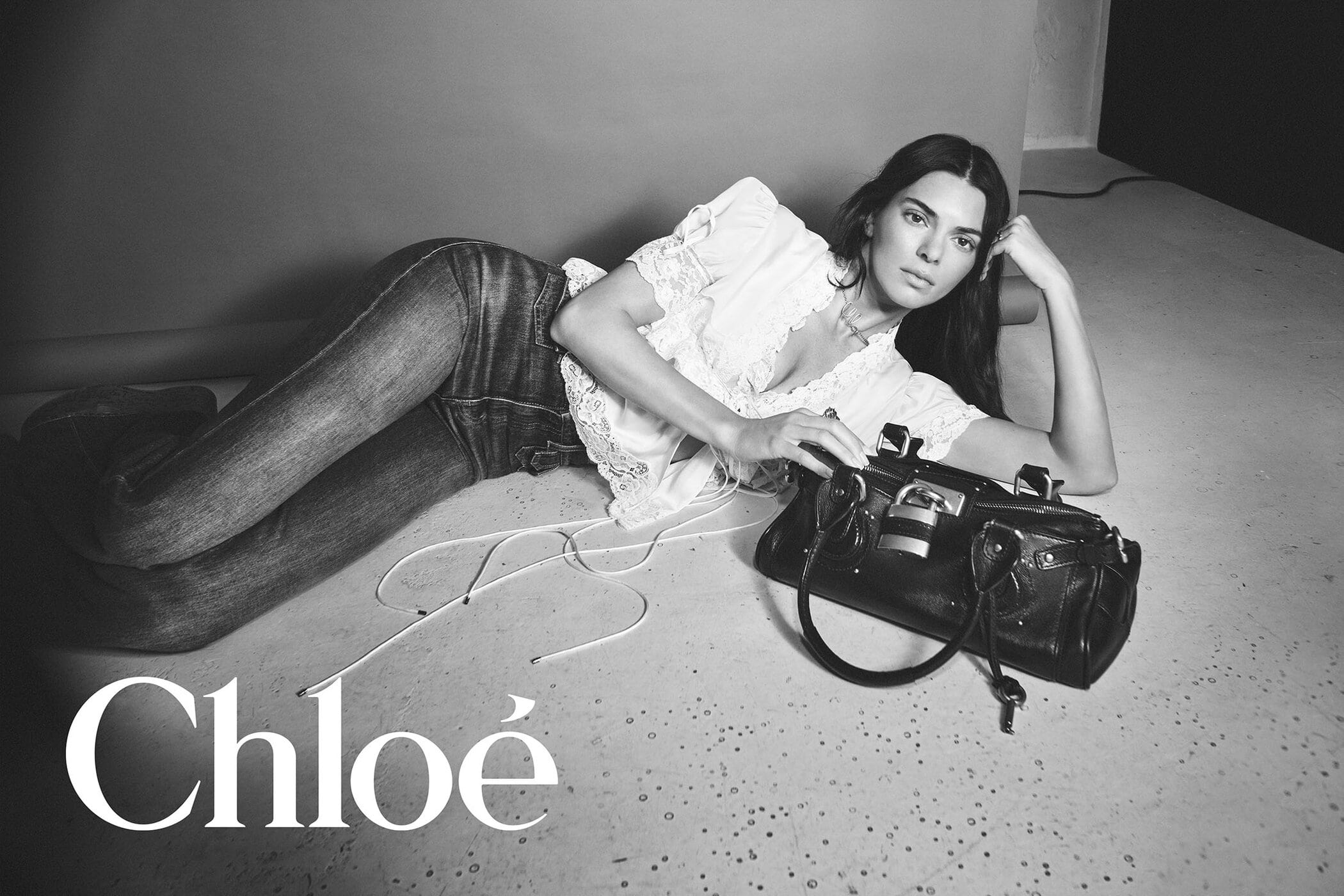 Kendall Jenner reclining on a studio floor with a black leather handbag for Chloé Paddington Bag campaign