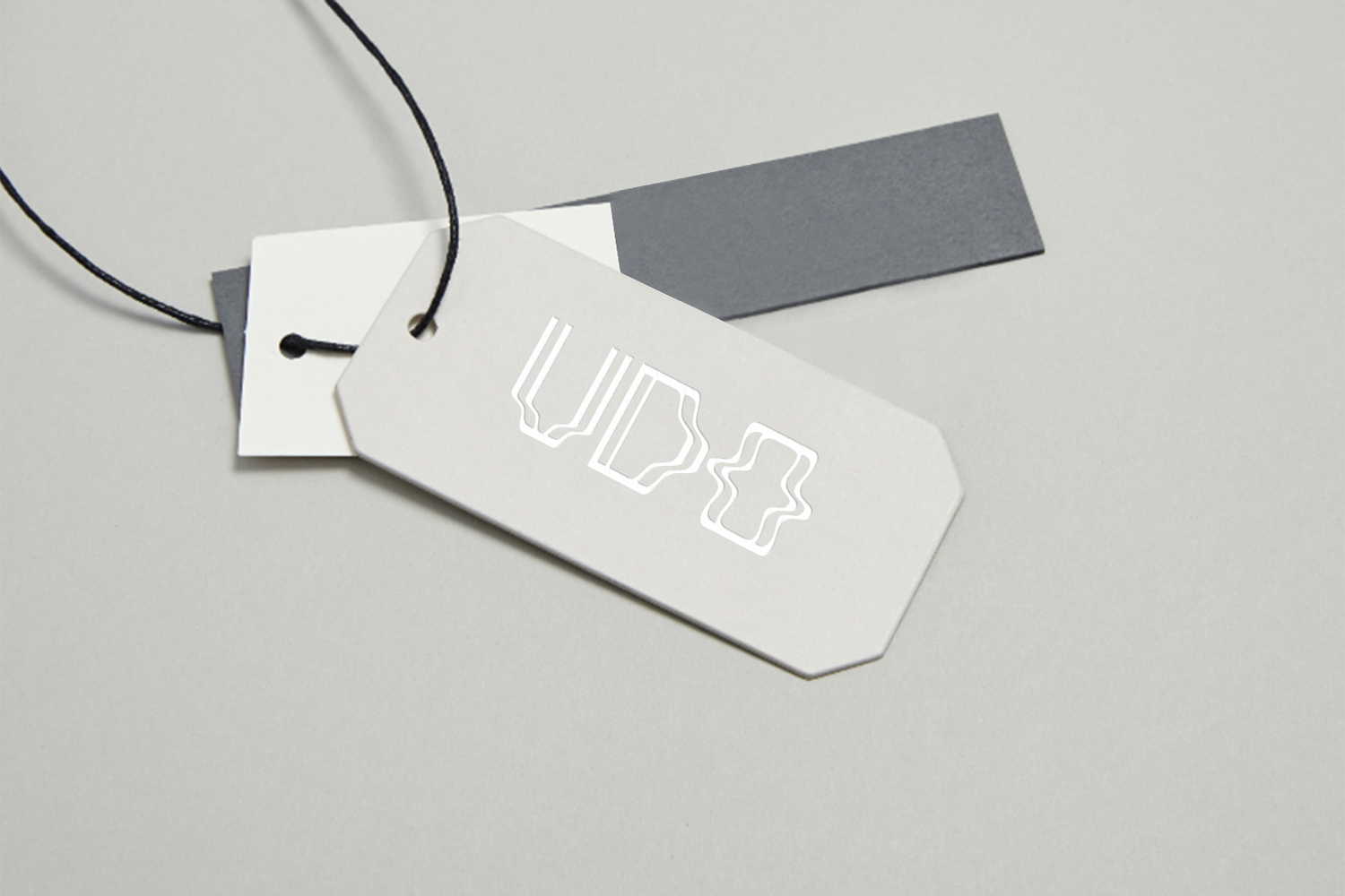 Close-up of a light grey product tag with silver debossed UDO logo attached to black string over stacked paper swatches