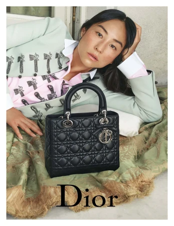 Greta Lee reclining on a green patterned blanket next to a black quilted Lady Dior handbag for Dior