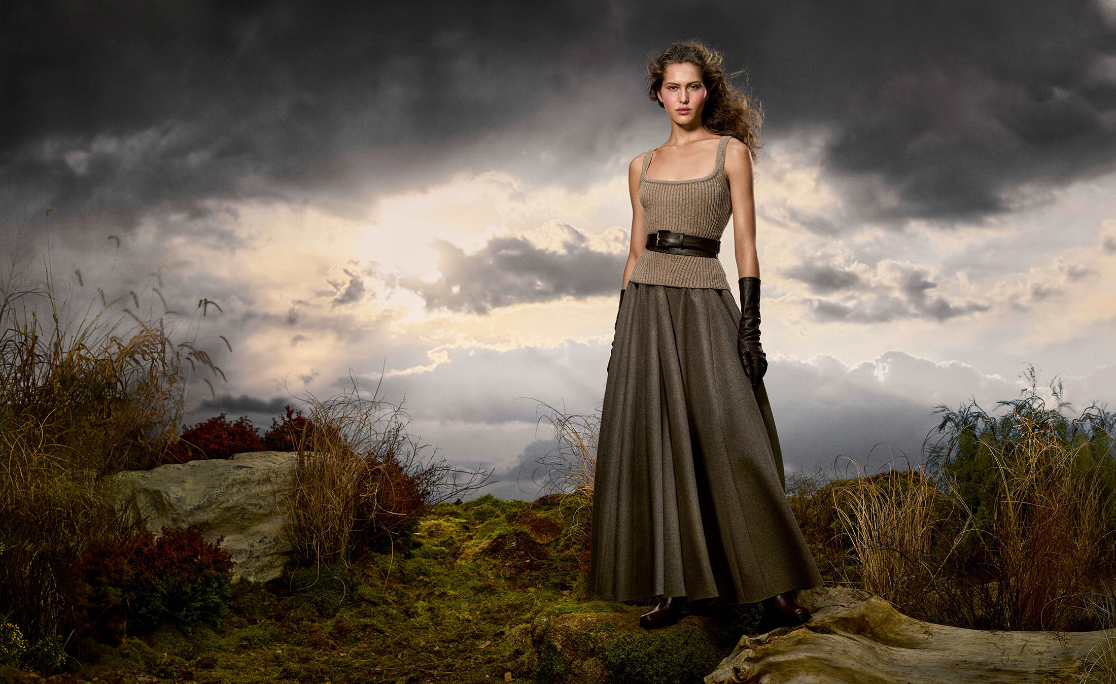Model wearing a ribbed knit top and long skirt standing outdoors against a dramatic cloudy sky backdrop.