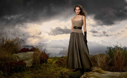 Model wearing a ribbed knit top and long skirt standing outdoors against a dramatic cloudy sky backdrop.