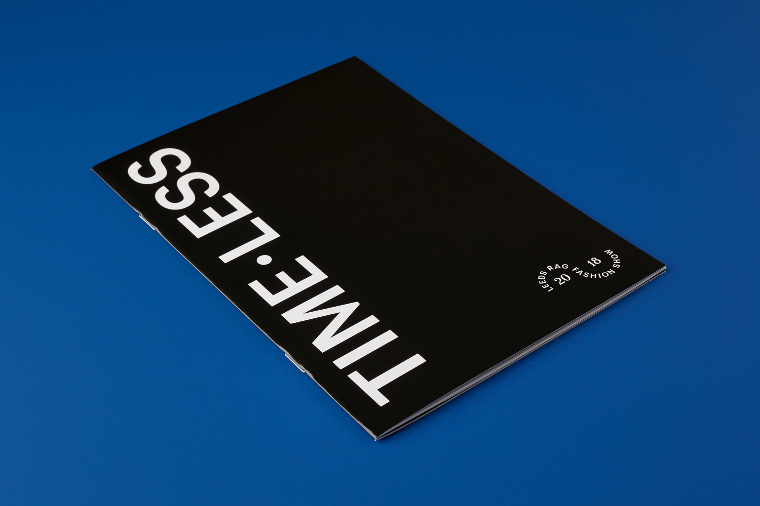 Black booklet with bold white typography reading TIMELESS resting on a vibrant blue surface