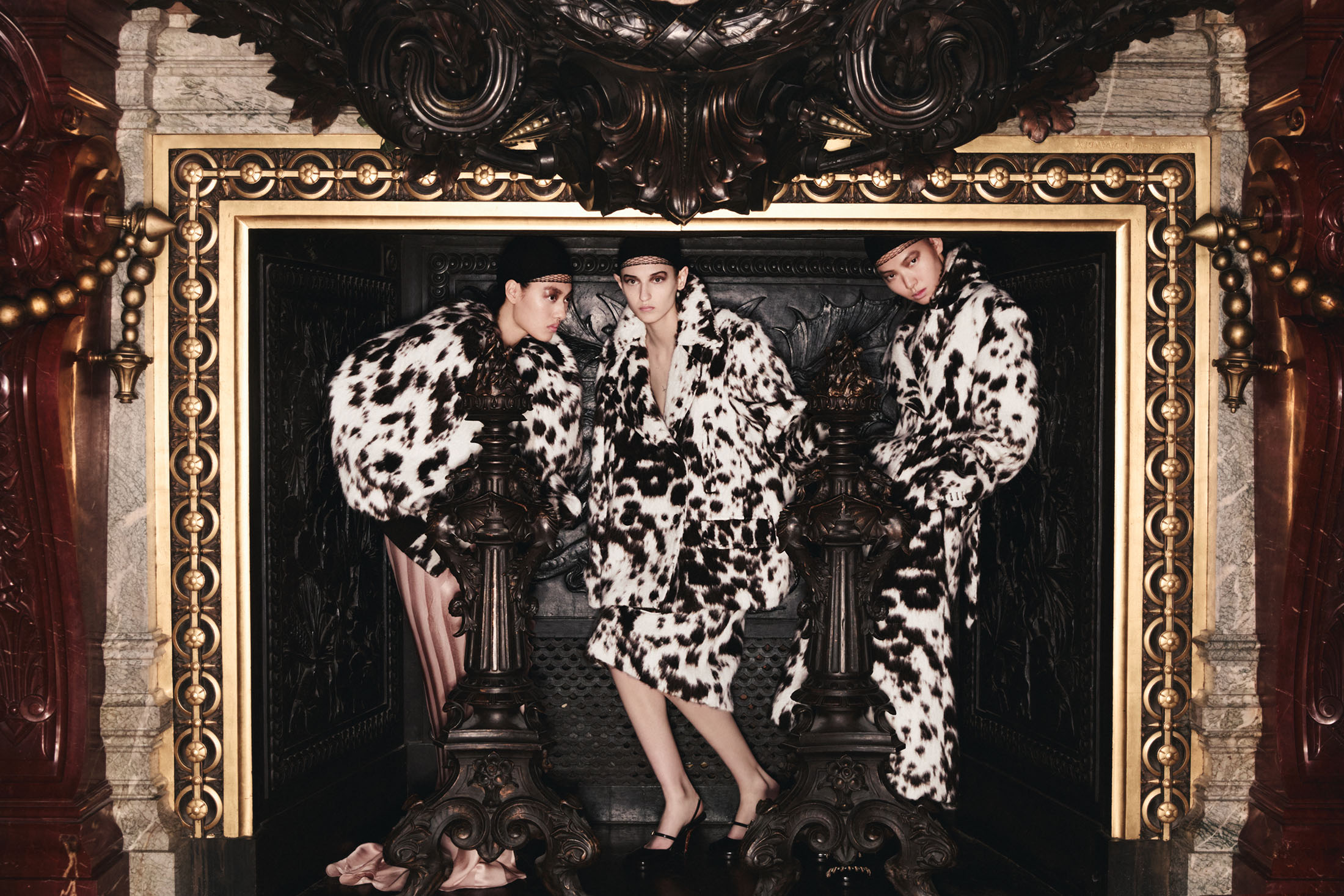 Three models wearing dalmatian print coats posing within an ornate dark architectural framework for Dries Van Noten