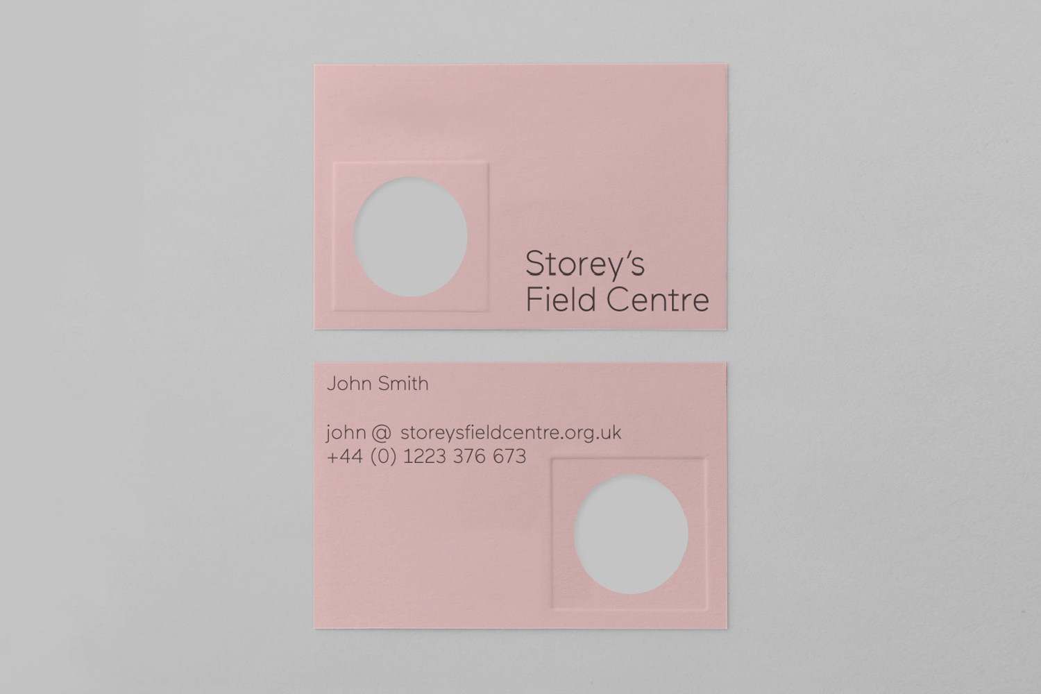 Pink business cards with debossed circular windows and typography for Storey's Field Centre on a grey background