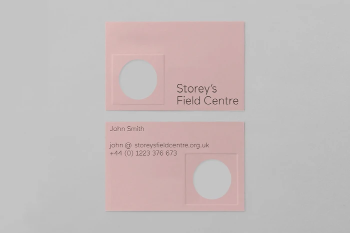 Pink business cards with debossed circular windows and typography for Storey's Field Centre on a grey background