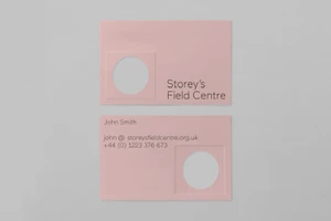 Pink business cards with debossed circular windows and typography for Storey's Field Centre on a grey background