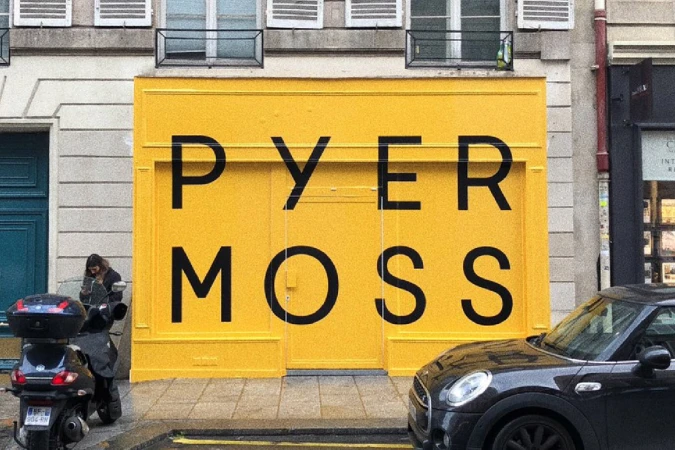 Bright yellow storefront facade featuring bold black PYER MOSS lettering on a city street with parked cars