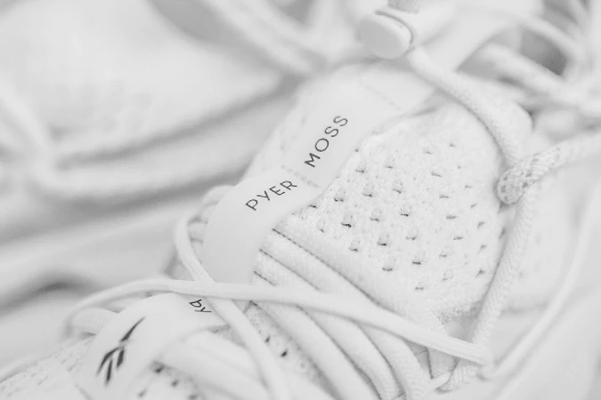 Macro shot focusing on the white sneaker lacing system and branding for Pyer Moss footwear.