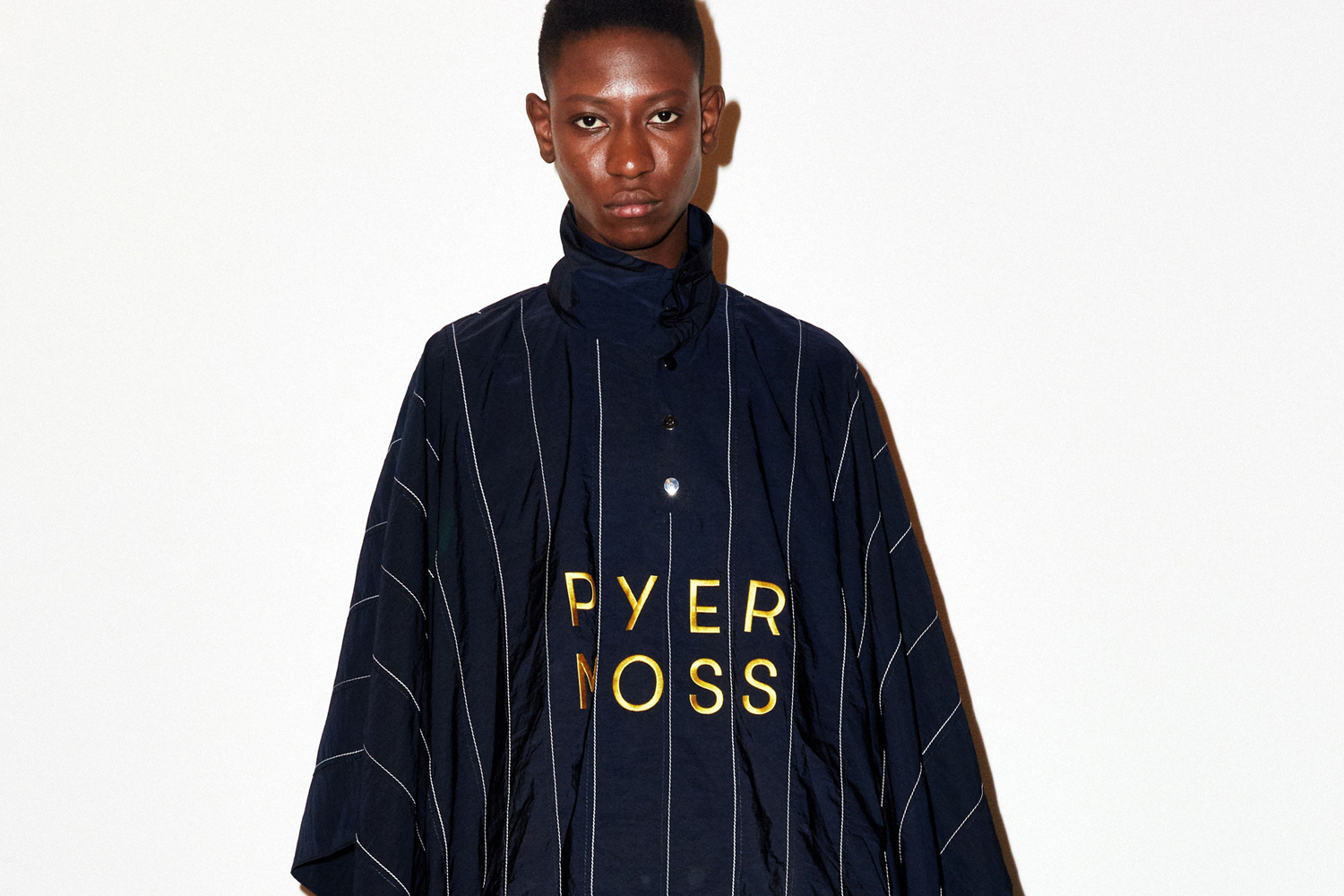Model wearing a dark pinstripe top with gold lettering against a plain white background