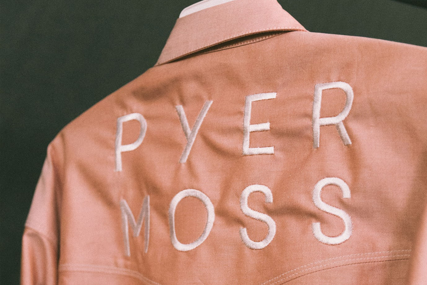 Close-up of the back of a pink Pyer Moss jacket featuring white embroidered lettering and visible fabric texture.