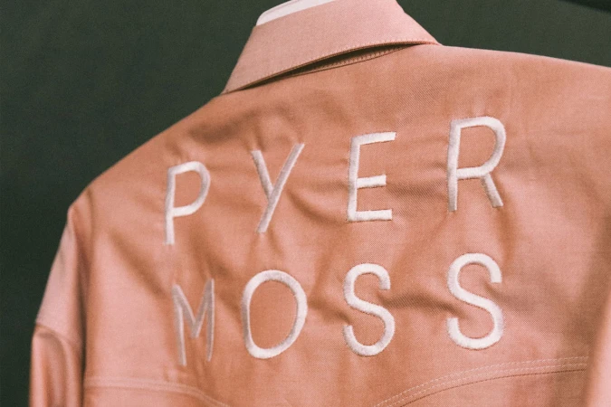 Close-up of the back of a pink Pyer Moss jacket featuring white embroidered lettering and visible fabric texture.