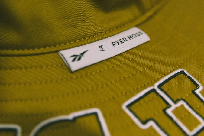 Close-up of mustard yellow bucket hat with white brand label and embroidered lettering