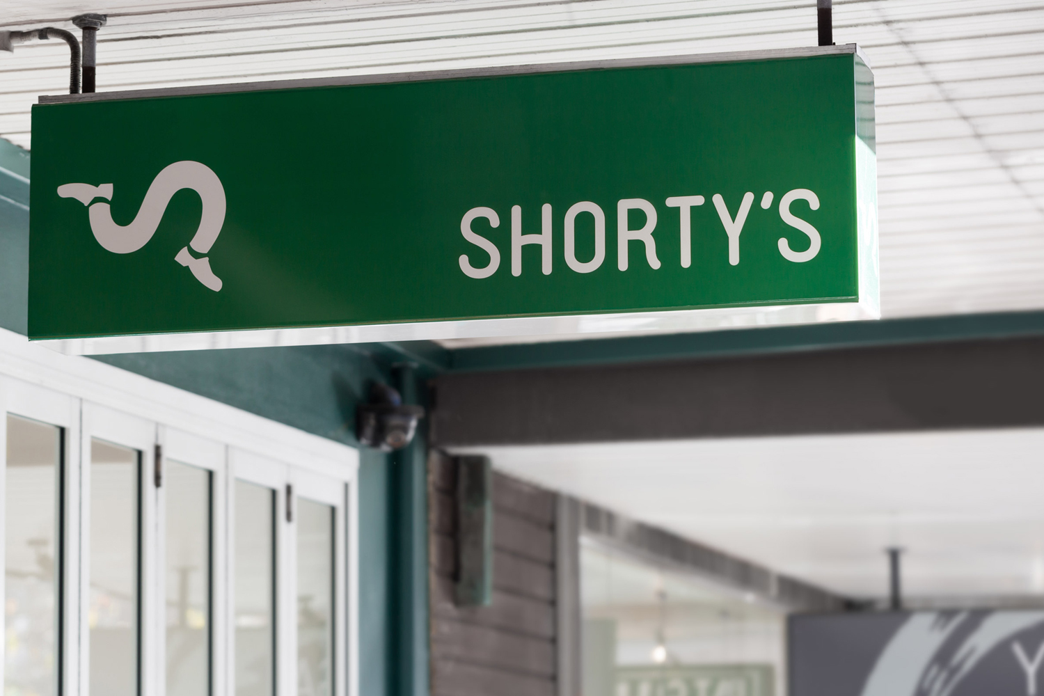 Green illuminated store sign reading Shorty's with a lowercase s shoe logo mounted outside a retail storefront