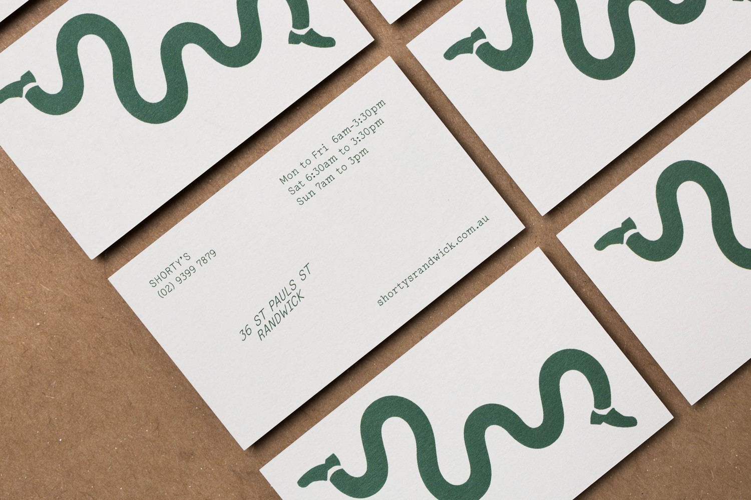 Multiple white business cards with a green wavy illustrative pattern and contact information arranged on brown paper