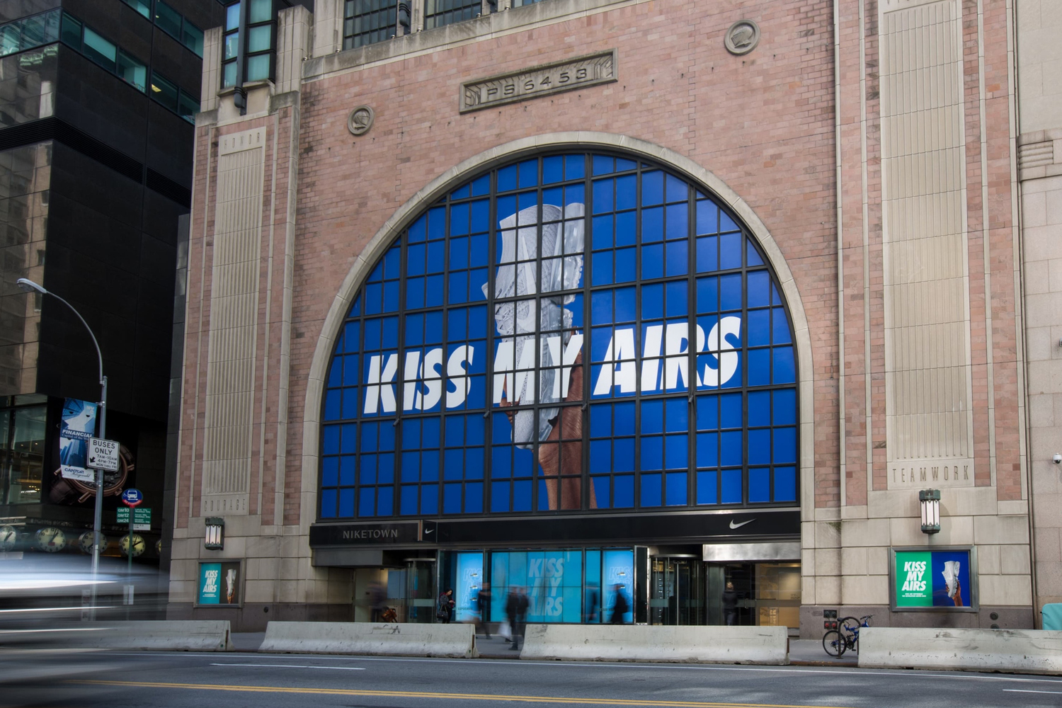 Nike store exterior featuring a large arched window with Kiss My Airs graphic display on a city street.