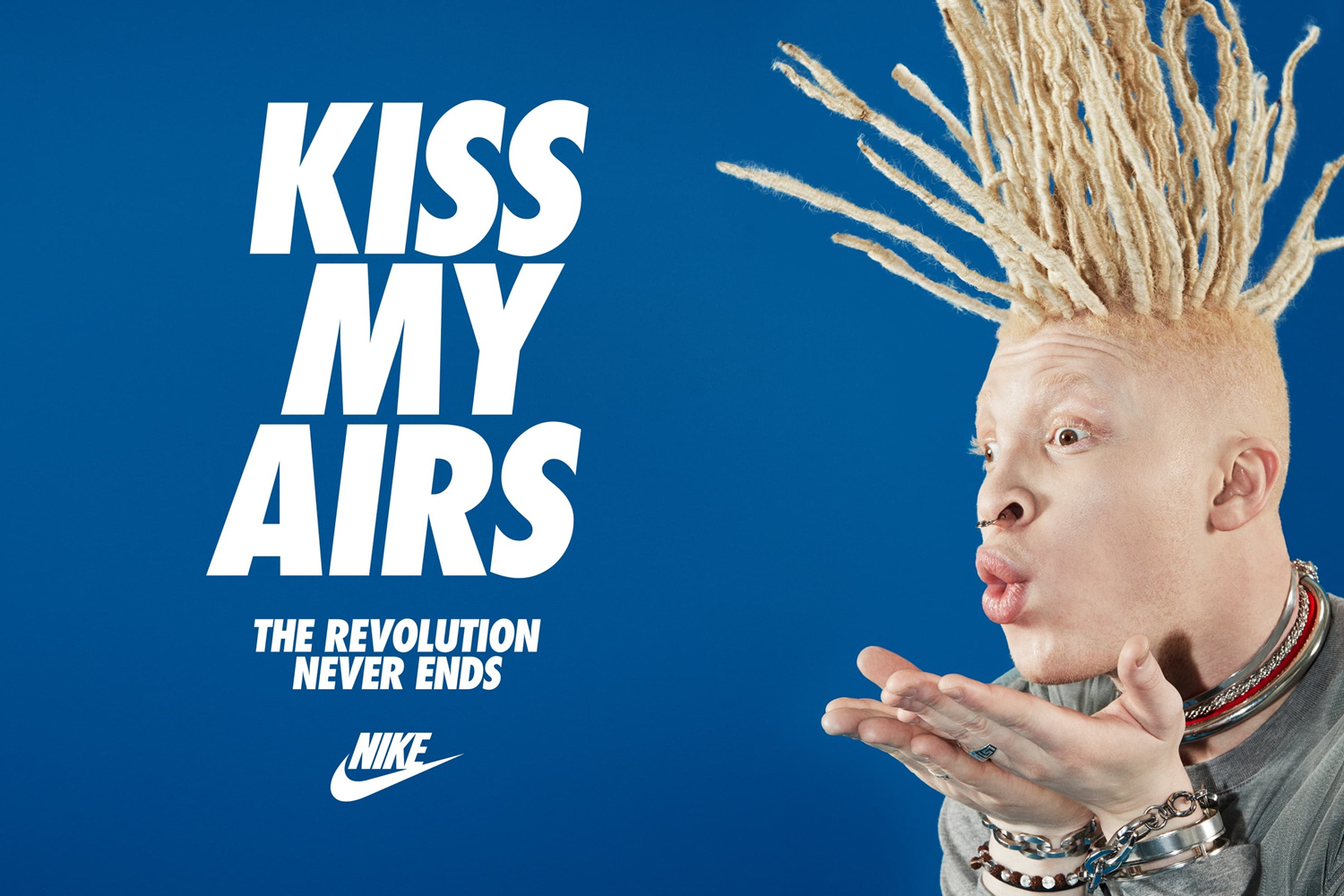 Close-up portrait of person with spiky blonde dreadlocks and nose ring blowing a kiss against a blue background for Nike brand identity